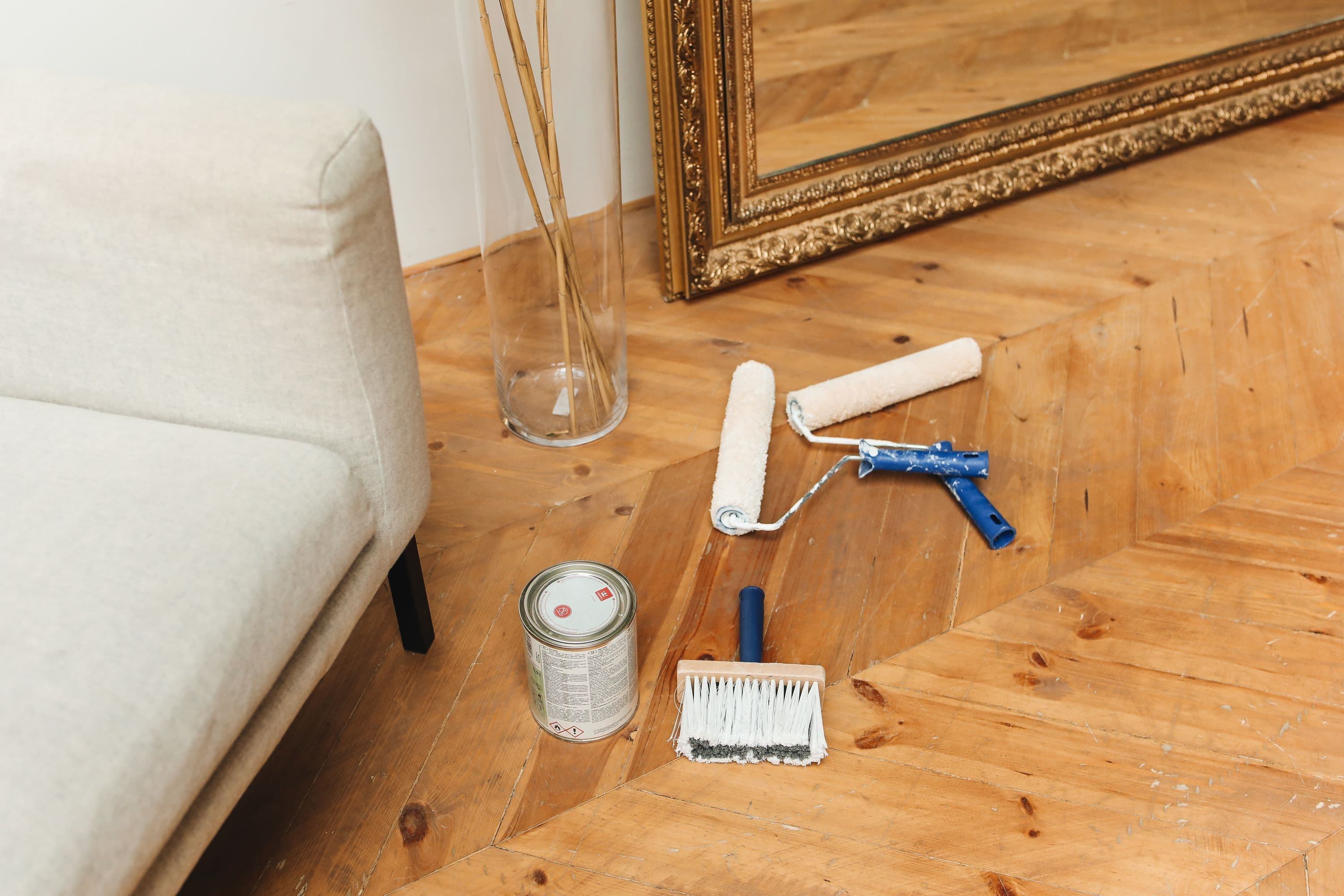 Paint rollers, a tin and a brush laid on a parquet floor in a furnished living room